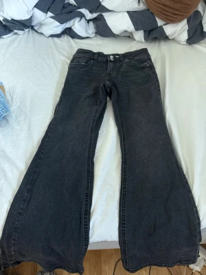 Svarta utsvängda jeans - Säljer ett par svarta jeans med låg midja och riktigt breda utsvängda ben. Klassisk femficksmodell med dubbla silverknappar i midjan. Perfekta för dig som gillar en retro eller edgy stil. Materialet är denim i bomull.