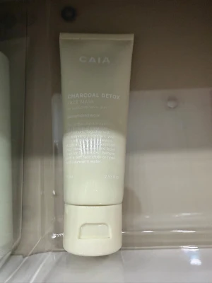 Charcoal Detox Face Mask från CAIA - En ansiktsmask i tub från CAIA med detox-effekt, innehållande aktivt kol. Tuben är ljusbeige med vit text och har en praktisk snäpplock. Perfekt för dig som vill rengöra huden på djupet och få en fräsch känsla.använd ca 3 gånger