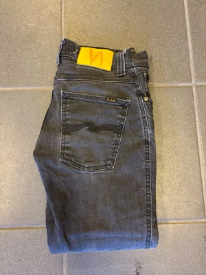 Nudie Jeans W27 – mörkgrå/svart tvätt - Snygga jeans från Nudie Jeans i mörkgrå/svart tvätt med lätt slitna detaljer för en snygg vintagekänsla. Klassisk 5-ficksmodell med Nudies karakteristiska söm på bakfickorna. Bekväm passform och stretchig denim som sitter fint. 📏 Storlek: W27 🎨 Färg: Mörkgrå/svart ✅ Bra skick, se bilder för detaljer 👖 Perfekta till både vardag och festligare tillfällen Skickas snabbt eller hämtas enligt överenskommelse. #nudiejeans #jeans #w27 #denim #svartajeans #vintage #s