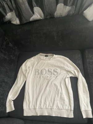 Hugo boss tröja - Vit stickad tröja från Hugo Boss med stor BOSS-logga och texten HUGO BOSS broderat framtill. Tröjan har rund halsringning, långa ärmar och ribbade muddar vid ärmslut och nederkant. Enkel och stilren design som passar till mycket.