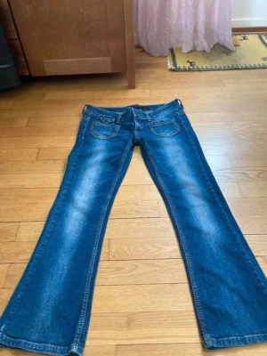 Blå kågmidjade bootcut jeans  - Säljer ett par blå bootcut jeans med snygga slitningar framtill och bakfickor. Jeansen har klassisk femficksmodell och är tillverkade i denim med lätt stretch. Perfekta för dig som gillar en avslappnad men trendig look.