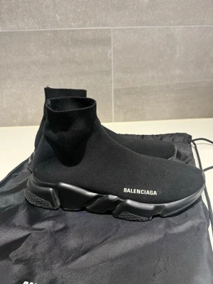 Balenciaga Speed Trainer svarta sneakers - Svarta Balenciaga Speed Trainers i storlek 42. Skorna är köpta från Miinto 2023, har orderbekräftelse på min mejl. Skorna är i överlag i gott skick även om de är använda. Dock håller bokstaven B på att lossna från märket på ena skon (se bild). Skorna kan fräschas upp antingen hemma med rätt produkter eller hos sneakerstvätten inne i stan eller likande butiker. Balenciaga påse medföljer även!