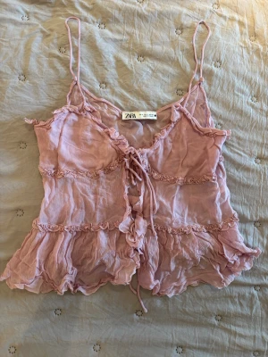 Ljusrosa linnetopp från Zara - Supersöt ljusrosa linnetopp från Zara med tunna axelband, volangdetaljer och snörning framtill. Toppen har en luftig och romantisk look med rynkade sömmar och lätt transparent tyg. Perfekt för varma dagar och att styla lager på lager.