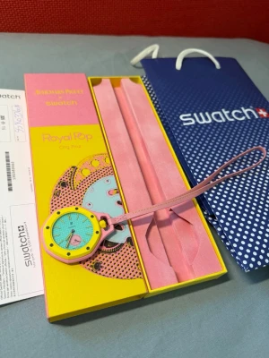Swatch Royal Pop Audemars Piguet - Swatch x Audemars Piguet Royal Pop Org Roz klocka med färgglad design i gult, rosa och blått. Klockan har en rund urtavla med synlig mekanik och texten 'Royal Pop' på glaset. Medföljer originalförpackning och handledsrem i rosa.