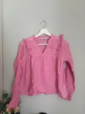 Rosa volangblus med v-ringning - Söt rosa blus v-ringning och volangdetaljer längs axlar och bröst