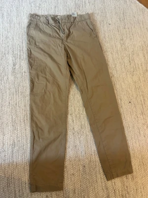 Beiga chinos med rak passform - Snygga beiga chinos med rak passform och klassisk design. Byxorna har sidofickor, bälteshällor och diskreta bakfickor. Tillverkade i ett mjukt bomullstyg som känns skönt mot huden. Perfekta för en clean och avslappnad stil. 