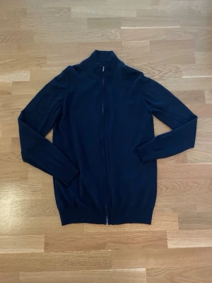 Mörkblå ziptröja från Riley - Snygg mörkblå ziptröja från Riley med hög krage och hel dragkedja framtill. Tröjan är stickad i ett mjukt material och har ribbade muddar vid ärmslut och nederkant. Perfekt för lager på lager och enkel att matcha med olika outfits.