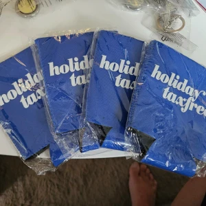 4 Blå burkhållare holiday taxfree - Säljer 4 blå burkhållare med texten 'holiday taxfree' i vitt. Tillverkade i mjukt tygmaterial och designade för att hålla drycken kall. Perfekt till stranden, picknick eller festival. Säljs i originalförpackning.
