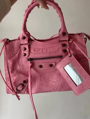 Rosa City Bag / Motorcycle Bag – Ny  - 🎀 Mått: • Bredd: 24 cm • Höjd: 15 cm • Djup: 8 cm  Väskan har flätade handtag, dekorativa dragkedjor, nitar och en matchande spegelberlock som ger den den klassiska city bag looken. 😊💕   Öppen för prisförslag!   