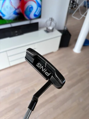 PING svart golfputter - Säljer en stilren svart golfputter från PING med klassisk form och tydlig vit linje för sikte. Skaftet är i metall och klubbhuvudet har en svart och blå detalj på träffytan. Perfekt för dig som vill förbättra ditt närspel på greenen. Kan bytas mot annan putter 