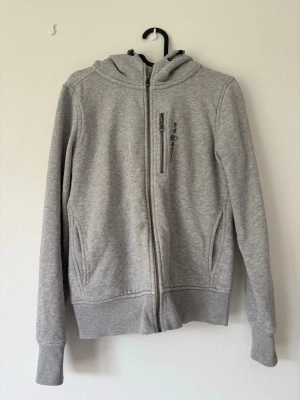 Ljusgrå zip hoodie från Oneill - Ljusgrå hoodie med dragkedja från Oneill. Tröjan har huva med dragsko, två sidofickor och en bröstficka med dragkedja. Tillverkad i mjukt sweatshirtmaterial och har ribbade muddar vid ärmar och nederkant. Perfekt för en avslappnad och sportig stil.