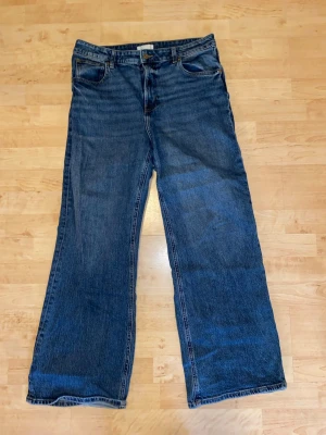 Blå raka jeans med fem fickor - Klassiska blå jeans med rak passform och fem fickor. Jeansen har normal midja, knappgylf och är tillverkade i slitstark denim. Perfekta för en avslappnad och tidlös stil.