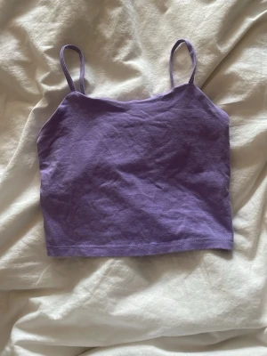 Lila croppad linne med smala band - Säljer ett lila croppat linne med smala axelband. Toppen har en enkel och stilren design, perfekt att matcha med jeans eller kjol. Materialet känns mjukt och lätt mot huden.