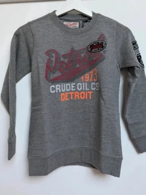 Ny grå sweatshirt från Petrol Industries  - Ny grå sweatshirt med tryck och broderade patches på bröstet och ena ärmen. Texten 'Detroit', 'Crude Oil Co' och '1973' i rött, vitt och orange ger en sportig vintagekänsla. Rund halsringning och ribbade muddar för extra komfort från Petrol Industries. Storlek 140.