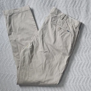 Beige chinos från Polo Ralph Lauren - Snygga beige chinos från Polo Ralph Lauren med klassisk rak passform. Byxorna har bälteshällor, knappstängning och bakficka med knapp och Polo-detalj. Tillverkade i mjukt bomullstyg som känns skönt mot huden.