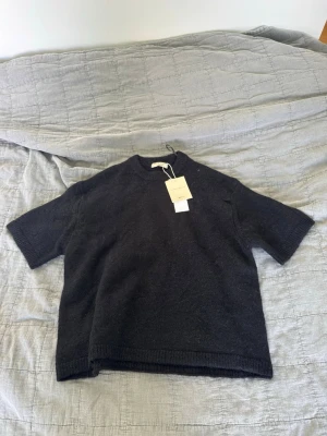 Svart stickad topp  - Säljer en svart stickad topp med korta ärmar och rund hals. Toppen har en enkel och stilren design, perfekt att matcha med olika outfits. Materialet känns mjukt och bekvämt mot huden.