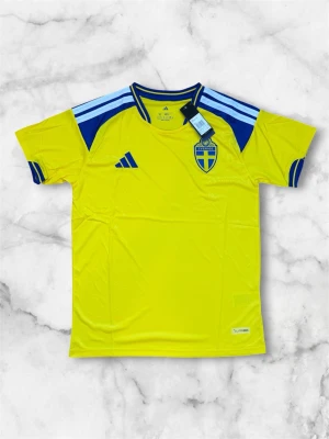 Sverige matchtröja Adidas gul/blå - Säljer en officiell Sverige matchtröja från Adidas i gult med blå detaljer och ljusblå ränder på axlarna. Tröjan har rund hals, korta ärmar och Sveriges landslagsemblem på bröstet. Tillverkad i lätt och ventilerande material, perfekt för fotboll eller träning.