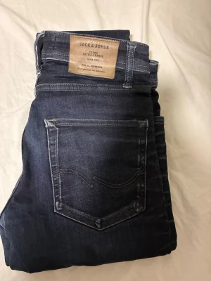Mörkblå jeans från Jack & Jones - Snygga mörkblå jeans från Jack & Jones med klassisk femficksdesign och kontrastsömmar. Jeansen har en patch i läderimitation bak i midjan och raka ben. Perfekta till en avslappnad streetstil.
