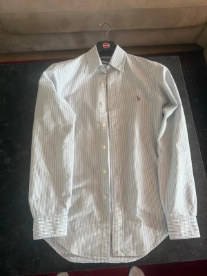 Ralph lauren oxford skjorta  - Säljer denna ljus blå vit randiga oxford skjortan från ralph lauren. Storleken är xs och den är regular fit. Skicket är så gott som nytt, enbart använd max 5 ggr. 