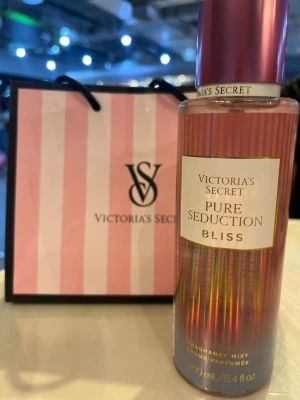 Victoria's Secret Pure Seduction Bliss - Victoria's Secret Pure Seduction Bliss är en doftmist i en cylinderformad flaska med rosa och skimrande detaljer samt ett matchande rosa lock. Flaskan rymmer 250 ml och har en elegant etikett med guldiga inslag. Perfekt för dig som gillar fräscha och feminina dofter. Helt ny.