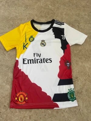 Multiklub fotbollströja Ronaldo - Cool fotbollströja med flera klubbars loggor, bland annat Real Madrid, Juventus, Manchester United och Sporting CP. Tröjan har Ronaldo och nummer 7 på ryggen, är kortärmad och har en mix av vitt, gult, svart och rött. Perfekt för dig som älskar fotboll och Ronaldo.
