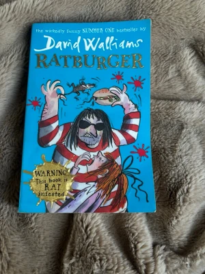 Ratburger av David Walliams - En humoristisk och fartfylld bok på engelska, 'Ratburger' av David Walliams, med färgstarkt illustrerat omslag av Tony Ross. Boken har ett blått omslag med tecknade figurer och råttor, och handlar om Zoe och hennes äventyr med sin husråtta.Old from my old school name of my school still in the back