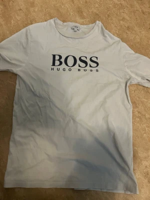 Vit t-shirt från Hugo Boss - Vit t-shirt från Hugo Boss med stort svart BOSS-tryck på bröstet. Klassisk rund halsringning och korta ärmar. Perfekt för dig som gillar stilrena och trendiga plagg med tydlig logga. Materialet är mjukt och känns skönt mot huden.