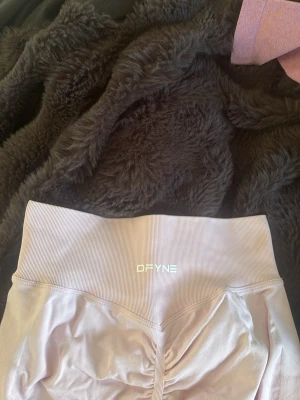 Ljusrosa träningstights-shorts Dfyne - Säljer ett par ljusrosa träningstights-shorts från DFYNE med hög midja och scrunch-detalj framtill. De är tillverkade i ett stretchigt syntetmaterial som sitter tight och bekvämt. Perfekta för gymmet eller andra träningspass!