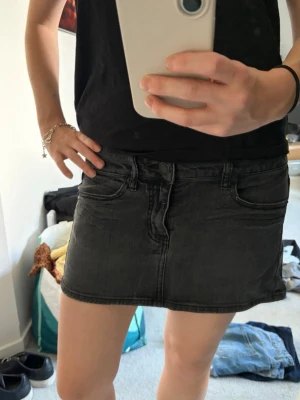 Svart jeanskjol  - Säljer en svart, kort jeanskjol. Kjolen har en enkel, rak passform och är perfekt för dig som gillar en stilren och avslappnad look. Passar till det mesta och är lätt att matcha med olika toppar. Står storlek 2. Passar mig som har S/M. Lågmidjad. 