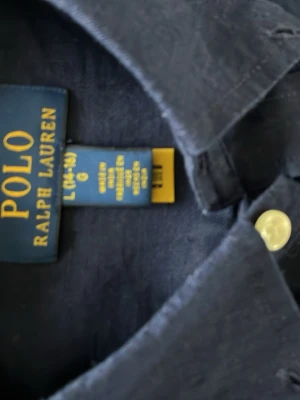 Mörkblå linneskjorta Polo Ralph Lauren - Snygg mörkblå skjorta från Polo Ralph Lauren i linne med klassisk krage och vita knappar. Skjortan har lång ärm och den ikoniska röda loggan broderad på bröstet. Perfekt för en stilren och avslappnad look.