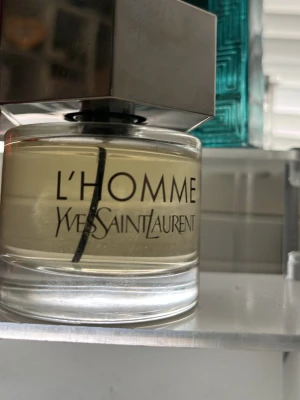 Yves Saint Laurent L'Homme parfym - Fräsch herrparfym från Yves Saint Laurent, L'Homme. Flaskan är rund i klart glas med en stor, sexkantig silverfärgad metallkork med YSL-logga på toppen. Doften är elegant och modern, perfekt för dig som gillar stilrena och exklusiva parfymer. Kan sänka priset 