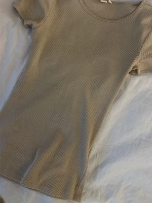 Beige ribbad topp från H&M - Säljer en beige ribbad topp från H&M med rund halsringning och korta ärmar. Toppen har en slim passform och är tillverkad i mjuk bomull, perfekt för en enkel och clean look.