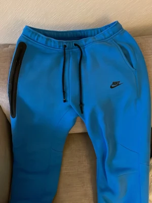 Blå Nike shorts med snörning - Ljusblå shorts från Nike med svart snörning i midjan och Nike-logga på vänster ben. Shortsen har sidofickor och är gjorda i mjukt material, perfekt för träning eller chill. Enkel och sportig design.