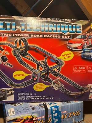 Multi-Technique bilbana racingspel - Säljer ett elektriskt bilbana racingspel från Multi-Technique med svart och gul bana, två bilar, loopar och hiss. Banlayouten är 285 x 153 cm och spelet har funktioner som Devil's Loop och elevator. Perfekt för dig som gillar fartfyllda bilspel och racing.
