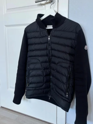 Svart pufferjacka från Moncler - Snygg svart pufferjacka från Moncler med quiltad front och ärmar i mjukt material. Jackan har två dragkedjeförsedda fickor, hög krage och Moncler-logga på ärmen. Perfekt för kalla dagar och ger en clean, modern look. Den passar inte mig längre därför säljer jag den. 