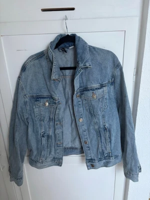 Oversized ljusblå jeansjacka - Säljer en oversized ljusblå jeansjacka med klassisk krage och två bröstfickor med knapp. Jackan har en avslappnad passform och silverfärgade knappar framtill. Perfekt att slänga över en hoodie eller t-shirt för en cool och avslappnad look.