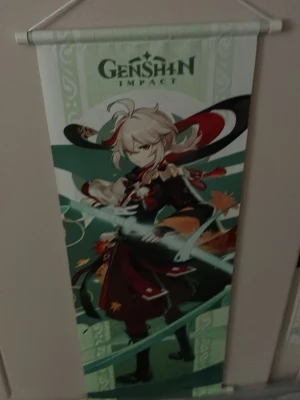Genshin Impact väggbonad Kazuha - Säljer en färgstark väggbonad med motiv från Genshin Impact, föreställande karaktären Kazuha. Bonaden har gröna, röda och vita toner och hängs upp med en vit plastpinne och snöre. Perfekt för dig som gillar anime och gaming.