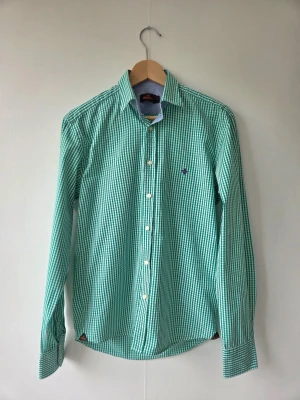 Morris mens shirt  - Snygg grön och vit rutig skjorta från Morris med klassisk krage och vita knappar framtill. Skjortan har lång ärm och en liten broderad logga i lila på bröstet. Perfekt för dig som gillar stilrena och fräscha skjortor.