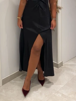 Svart långklänning med slits - Elegant svart långklänning med hög slits framtill och lätt rynkning vid midjan. Klänningen har en figurnära passform och är perfekt för dig som vill ha en stilren och klassisk look. Tillverkad i ett mjukt och följsamt material.