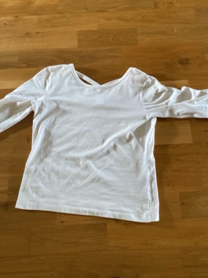 Vit långärmad topp med ett kors på ryggen. Lindex - Snygg vit långärmad topp. Tillverkad i mjuk bomull och har en enkel, clean look som passar till det mesta. Perfekt att styla med jeans eller kjol för en fräsch vibe. En liten fläck som knappt syns vid magen.