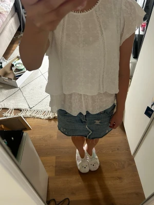 Vit spetsblus med korta ärmar - Söt vit blus i tunn spets med broderade detaljer och volangkant. Blusen har rund halsringning och korta ärmar med lätt rynk. Perfekt för en somrig och fräsch look. Ingen synlig logga eller märke.