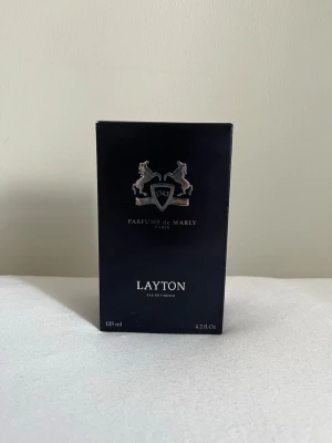 Parfums de Marly Layton EdP 125ml - Lyxig parfym från Parfums de Marly, Layton Eau de Parfum, 125 ml. Förpackningen är elegant och mörkblå med silverdetaljer och ett emblem med två hästar. Doften är känd för sin exklusiva och sofistikerade karaktär, tillverkad i Frankrike.