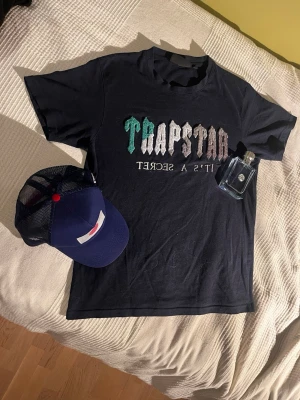 Trapstar svart t-shirt med tryck - Säljer en svart t-shirt från Trapstar med färgglatt broderat tryck på bröstet där det står 'Trapstar It's a Secret'. Tvättas och fixas för dig innan de kommer! Bara fråga om det skulle vara nåt! 