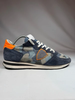 Philippe Model camo sneakers - Storlek 43 men passar 44. Snygga sneakers från Philippe Model med blått och grått camomönster, detaljer i mocka och en orange hälflik. Skorna har vita snören, vit sula och en ikonisk sköld på sidan. Perfekta för dig som gillar streetstyle och vill sticka ut.