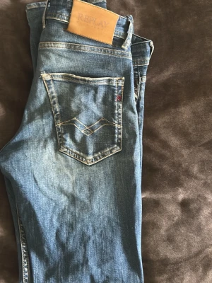 Blå Replay Grover straight fit jeans - Säljer ett par blå jeans från Replay, modell Grover med straight fit. Klassisk femficksdesign, snygga slitningar och kontrastsömmar. Tillverkade i denim med läderpatch bak i midjan. Perfekta för en avslappnad och trendig look.