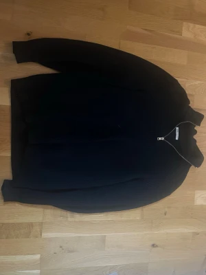 Svart stickad tröja med dragkedja Zara - Svart stickad tröja från Zara med halv dragkedja framtill och ribbad struktur. Tröjan har hög krage och långa ärmar, perfekt för lager på lager. Enkel och stilren design som passar till det mesta.