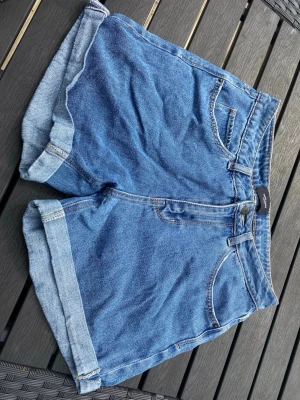 Blå denimshorts med uppvik - Säljer ett par klassiska blå denimshorts från Vero Moda med hög midja och uppvikta benslut. 