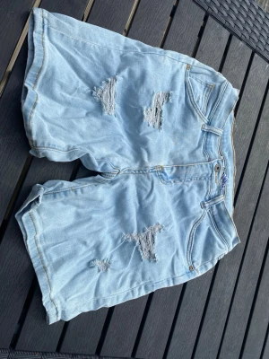 Ljusblå denimshorts med slitningar - Stretchiga jeansshorts med hål. Svag ljusröd fläck på höger bakficka 