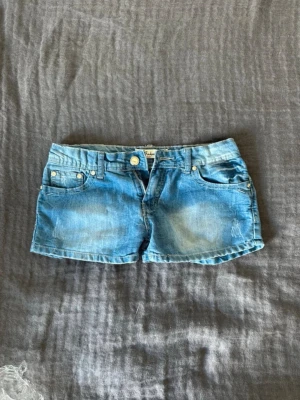 Ljusblå lågmidjade jeansshorts - Snygga ljusblå lågmidjade jeansshorts. Shortsen har en knapp och dragkedja framtill samt slitna detaljer för en avslappnad look. Perfekta för varma dagar och enkel att matcha med olika toppar.