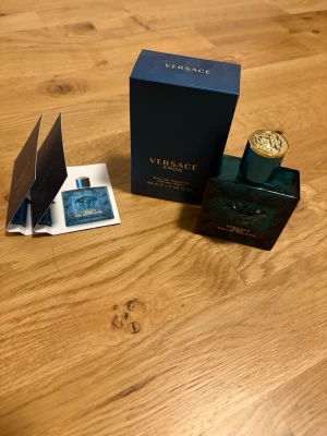 Versace Eros perfym - Har använt ungefär 10ml av flaskan 40ml återstår Versace Eros Eau de Toilette i en elegant, mörk turkos glasflaska med gulddetaljer och klassisk Versace-logga på locket. Flaskan har en fyrkantig form och kommer med originalkartong och provdoft. En ikonisk doft för dig som gillar lyxiga parfymer.  2 samples ingår 